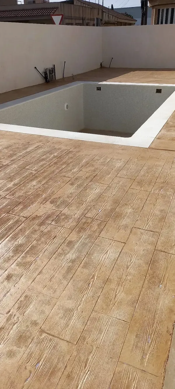 Una piscina vacía en un patio en construcción, rodeada de hormigón sin terminar.