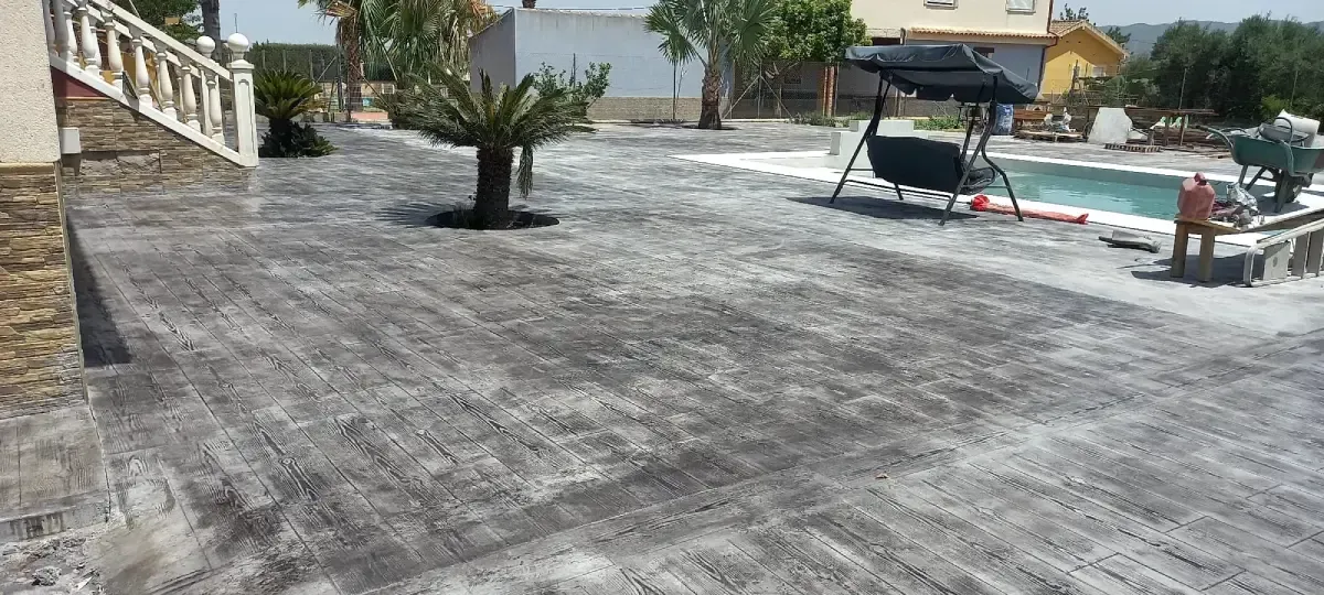 Patio exterior con palmera, piscina y columpios. Nublado.