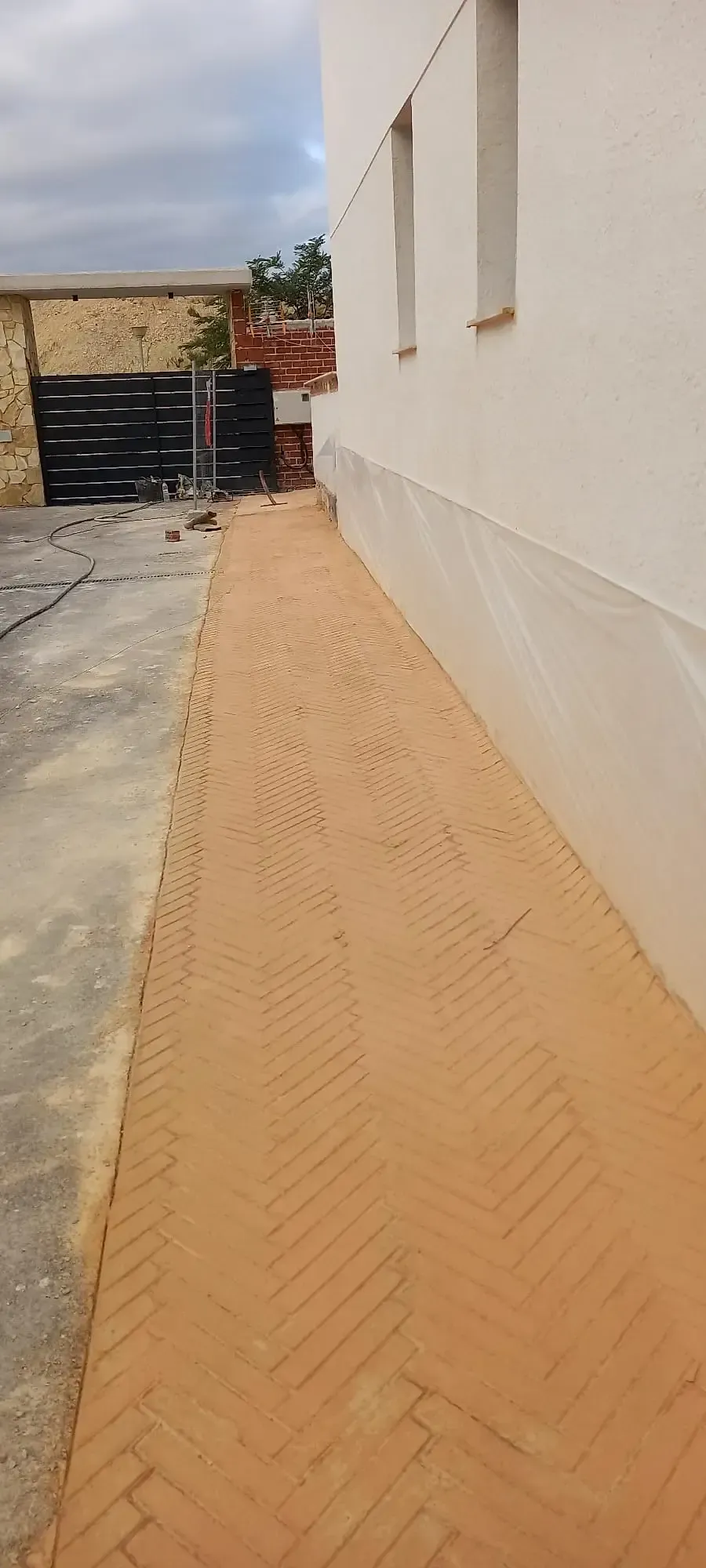 Camino estrecho de ladrillos al lado de un edificio blanco; el camino está hecho de ladrillos con diseño en espiga.