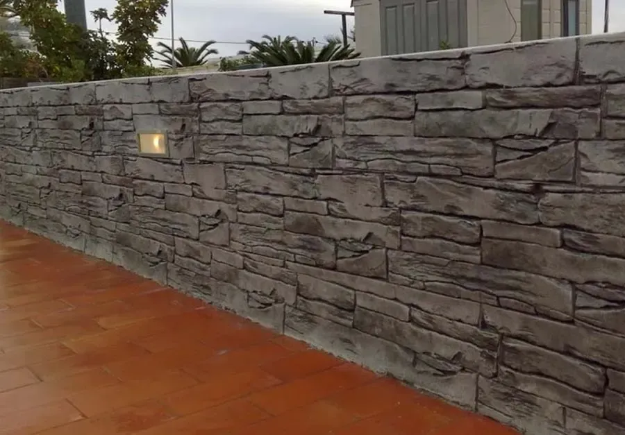 Pared con textura de piedra y luz empotrada sobre superficie pavimentada con ladrillo.