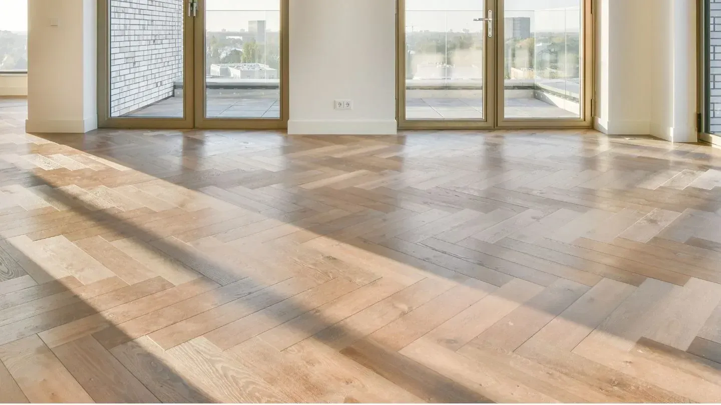Suelo de parquet de madera clara con luz solar que entra a través de puertas de cristal.