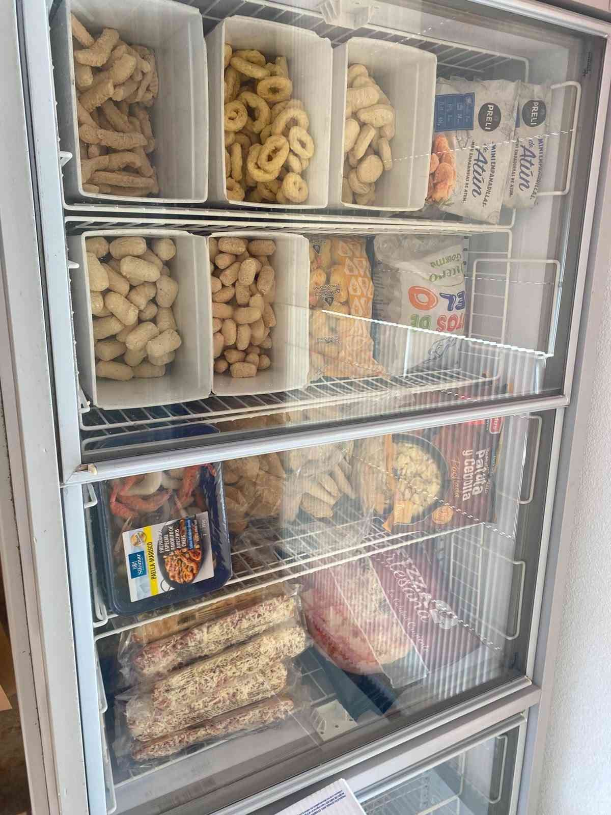 Vitrina de cristal con congelador surtido de aperitivos y alimentos envasados en estantes de alambre.