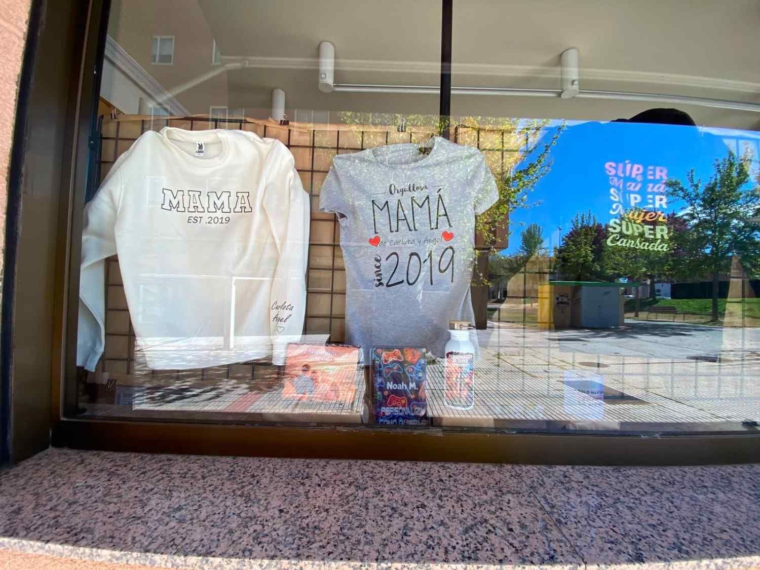 Exhibición en el escaparate con una sudadera blanca, una camiseta gris y una camiseta azul estampada.