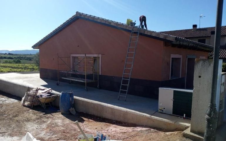Exterior de una casa con una escalera en el tejado y materiales de construcción en el patio