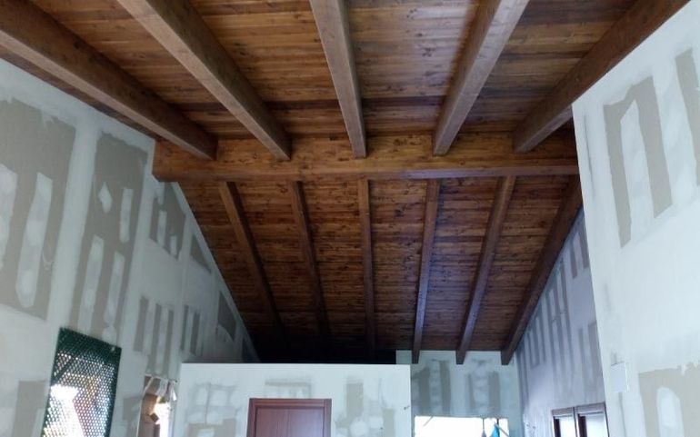 Techo abovedado de madera en una habitación sin terminar, con vigas a la vista y paredes de paneles de yeso irregulares