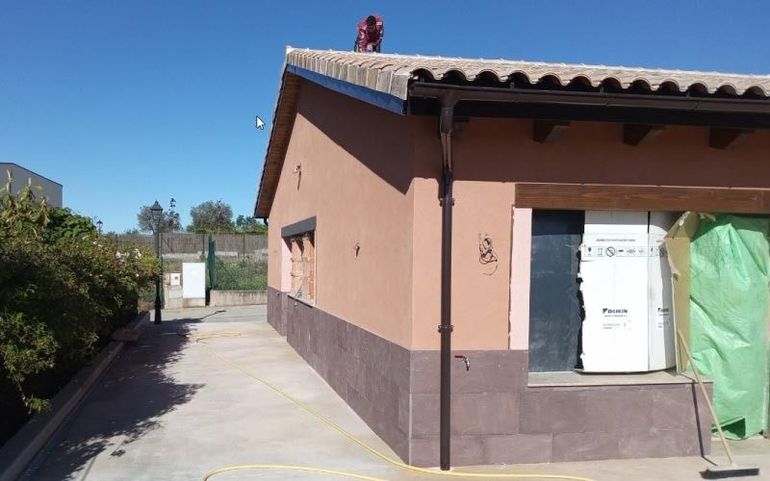 Exterior de una casa color melocotón con una puerta blanca, junto a un camino de entrada estrecho, con arbustos y una valla a los lados
