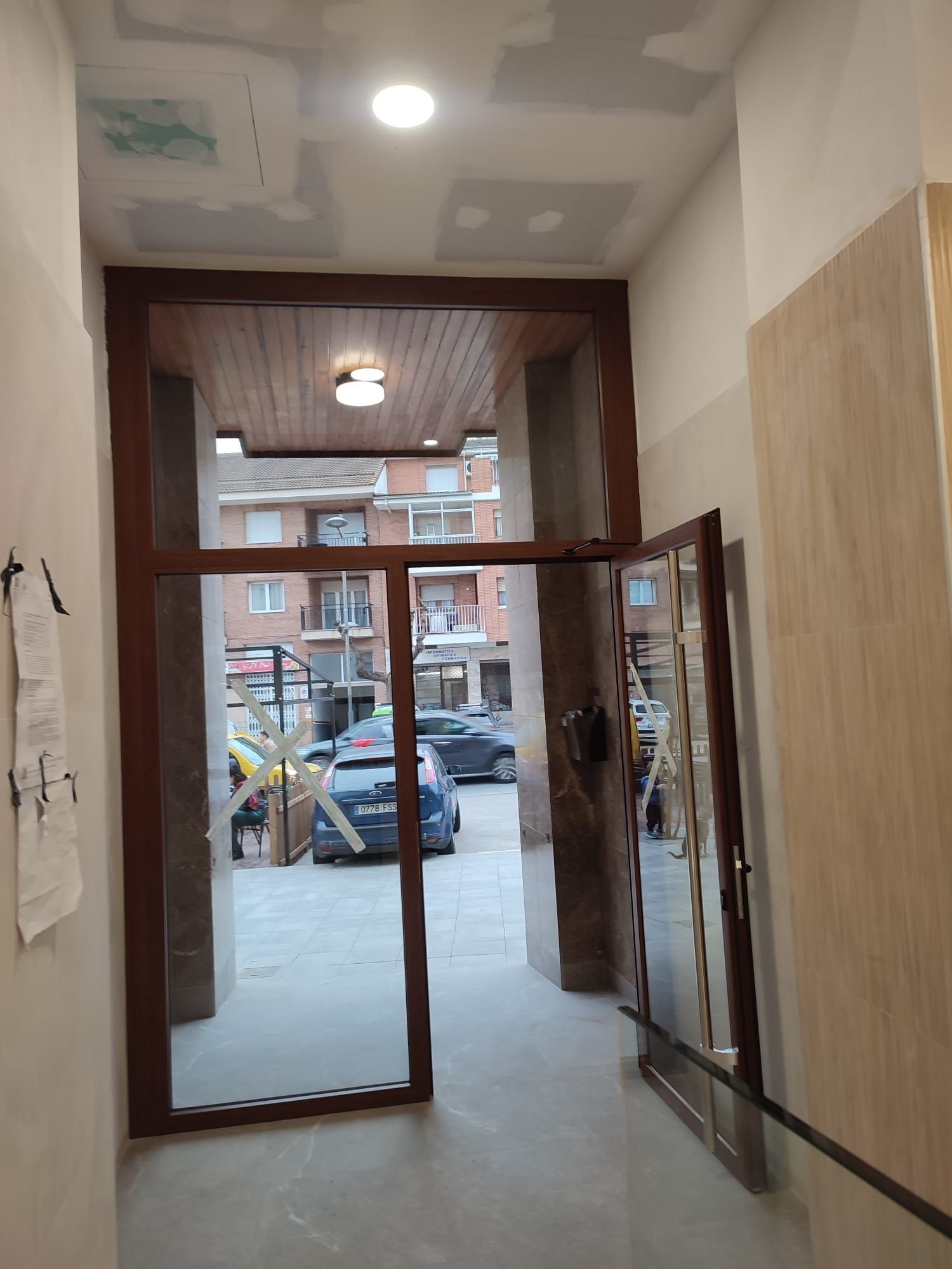 Entrada principal abierta con puertas de cristal que dan a una calle con coches aparcados y edificios.