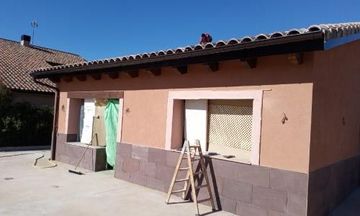 Exterior de una casa beige de una sola planta, con contraventanas blancas, una ventana pequeña y una escalera en el patio delantero.