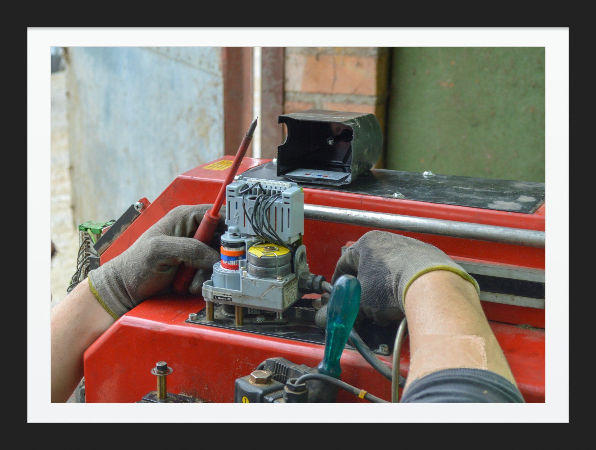 Manos con guantes trabajando en una máquina roja con un destornillador, probablemente reparándola.