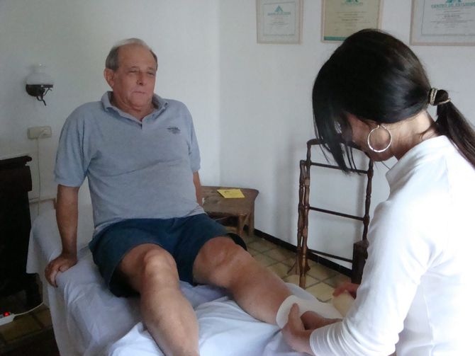 Un fisioterapeuta realiza un masaje en la parte inferior de la pierna de una persona sentada en un entorno clínico.