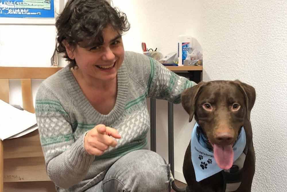 Eine Frau kniet neben einem braunen Hund, der ein blaues Halstuch trägt.