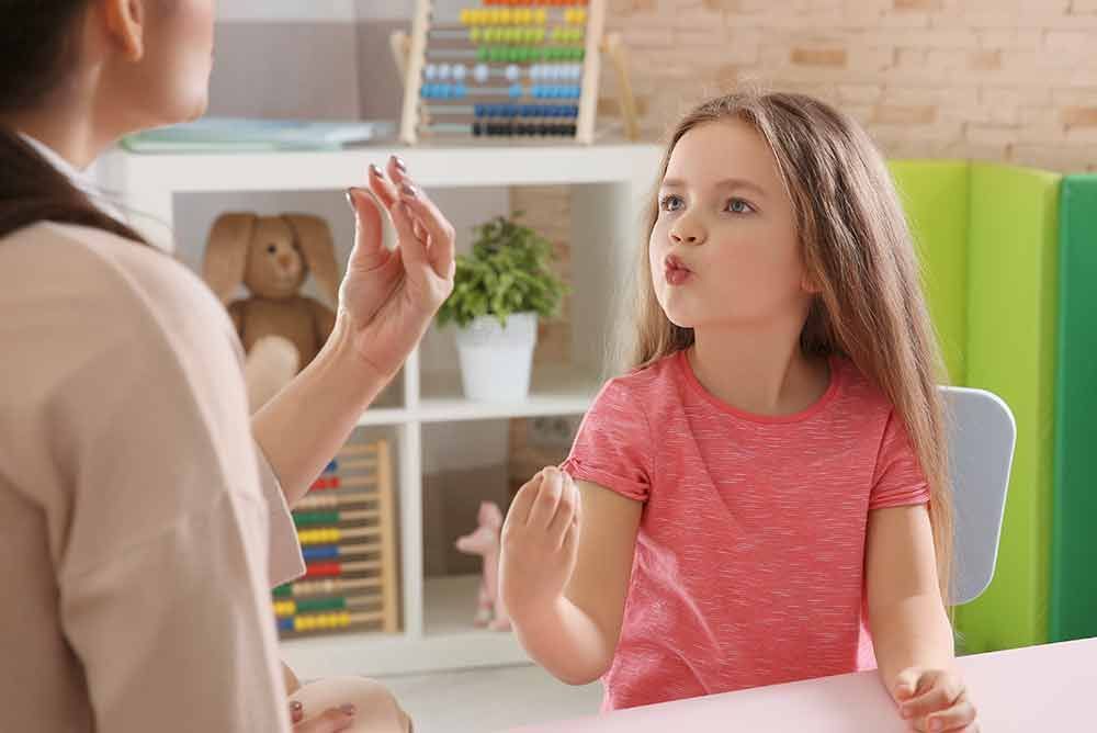 Ein kleines Mädchen sitzt an einem Tisch und unterhält sich mit einer Frau.