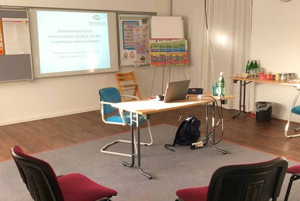 Ein Klassenzimmer mit Tisch und Stühlen und einer Projektionsleinwand.