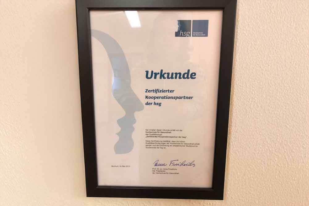 Ein Zertifikat mit der Aufschrift „Urkunde“ hängt an der Wand