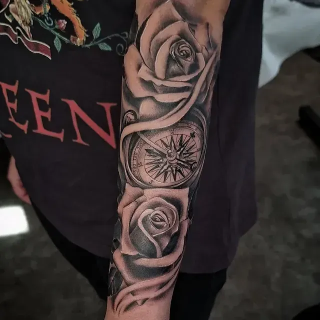 Eine Person hat ein Tattoo mit Rosen und einem Kompass auf dem Arm