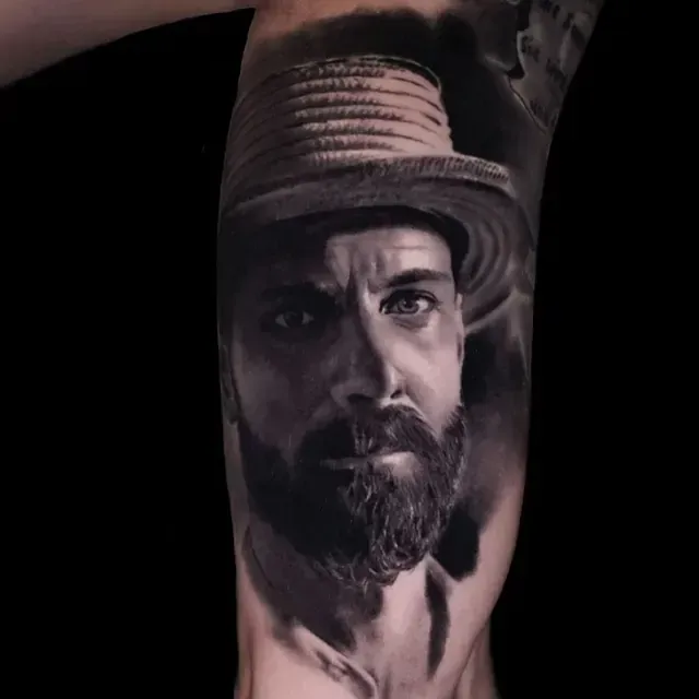 Ein schwarz-weißes Tattoo eines Mannes mit Bart und Hut.