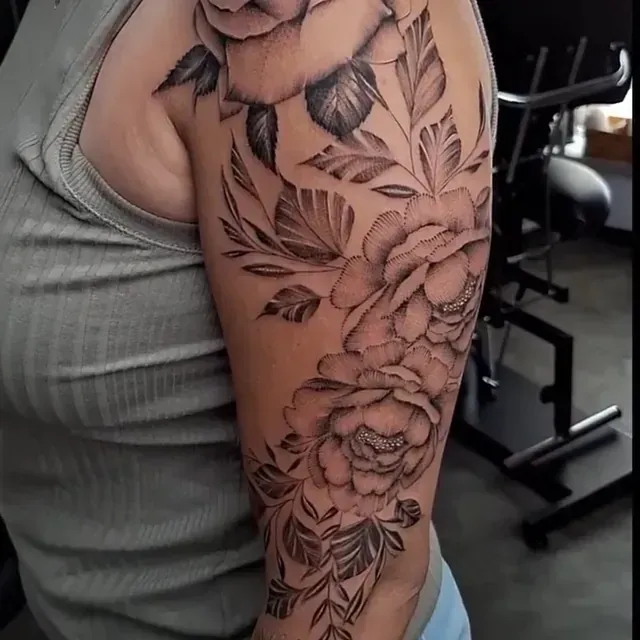 Eine Frau hat eine Tätowierung aus Rosen und Blättern auf ihrem Arm