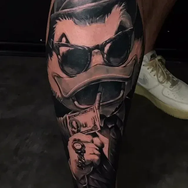 Eine Person hat eine Tätowierung einer Ente, die einen Dollarschein hält.