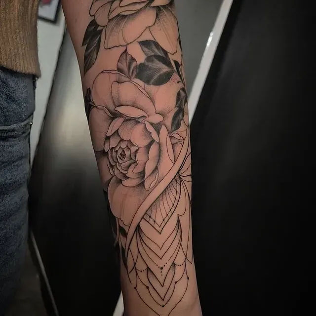 Eine Frau hat eine Tätowierung mit Rosen und Blättern auf ihrem Unterarm.