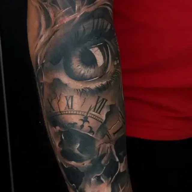 Ein Mann hat ein Auge und eine Uhr auf seinem Unterarm tätowiert.