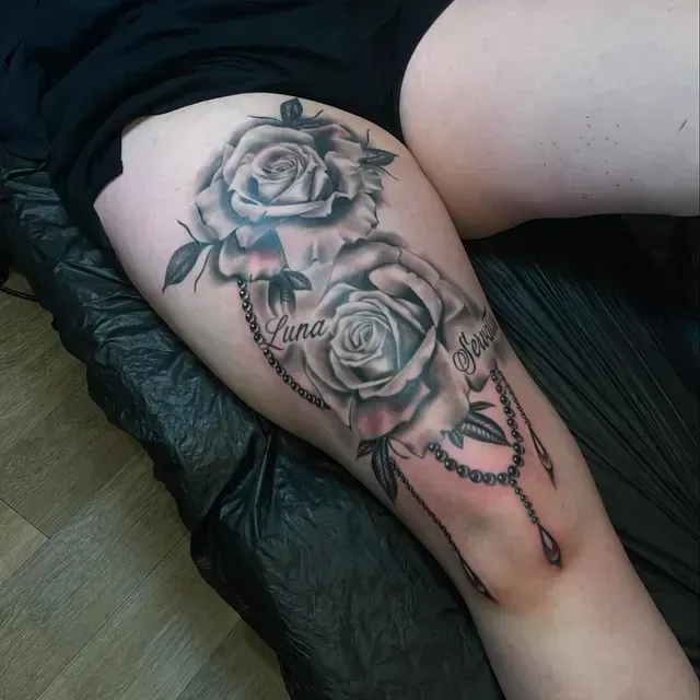 Eine Frau hat ein Tattoo von zwei Rosen und dem Namen Jana auf ihrem Bein