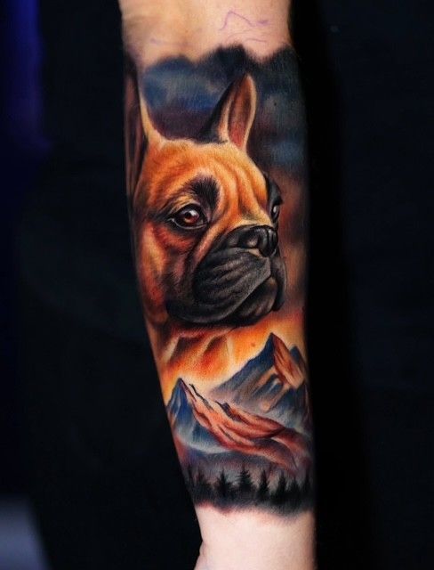 Unterarm-Tattoo einer französischen Bulldogge vor einer Berglandschaft in warmen Orange- und Schwarztönen