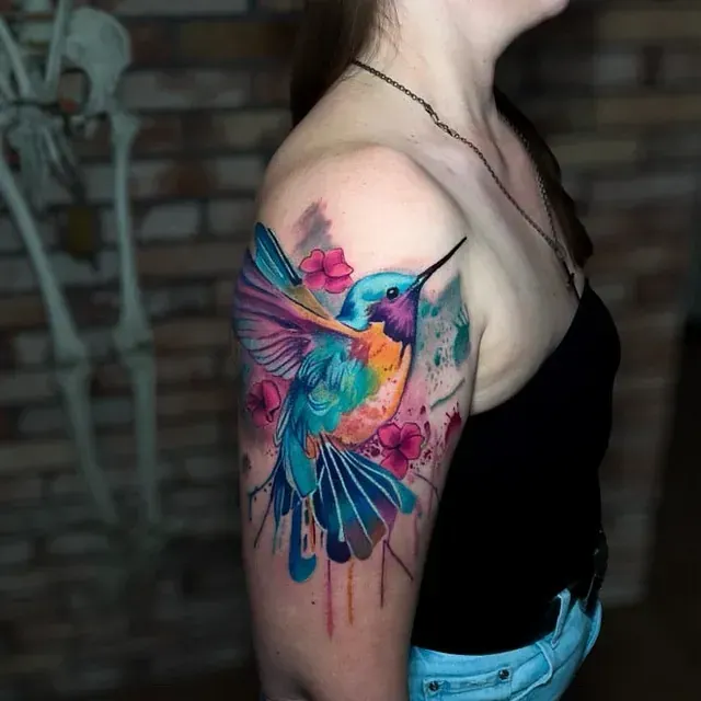 Eine Frau hat ein buntes Kolibri-Tattoo auf ihrem Arm