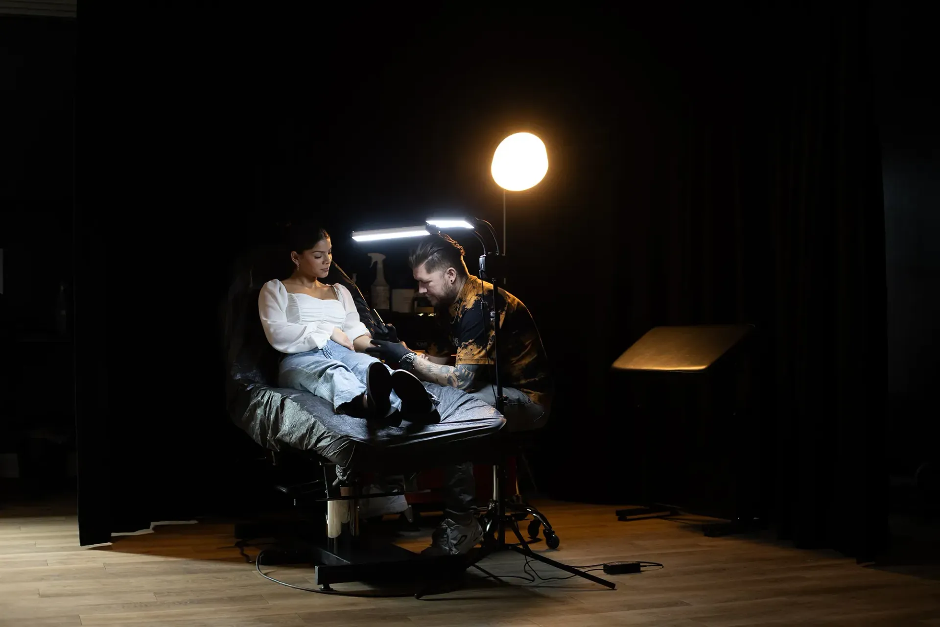 Ein Mann tätowiert in einem dunklen Raum den Arm einer Frau.