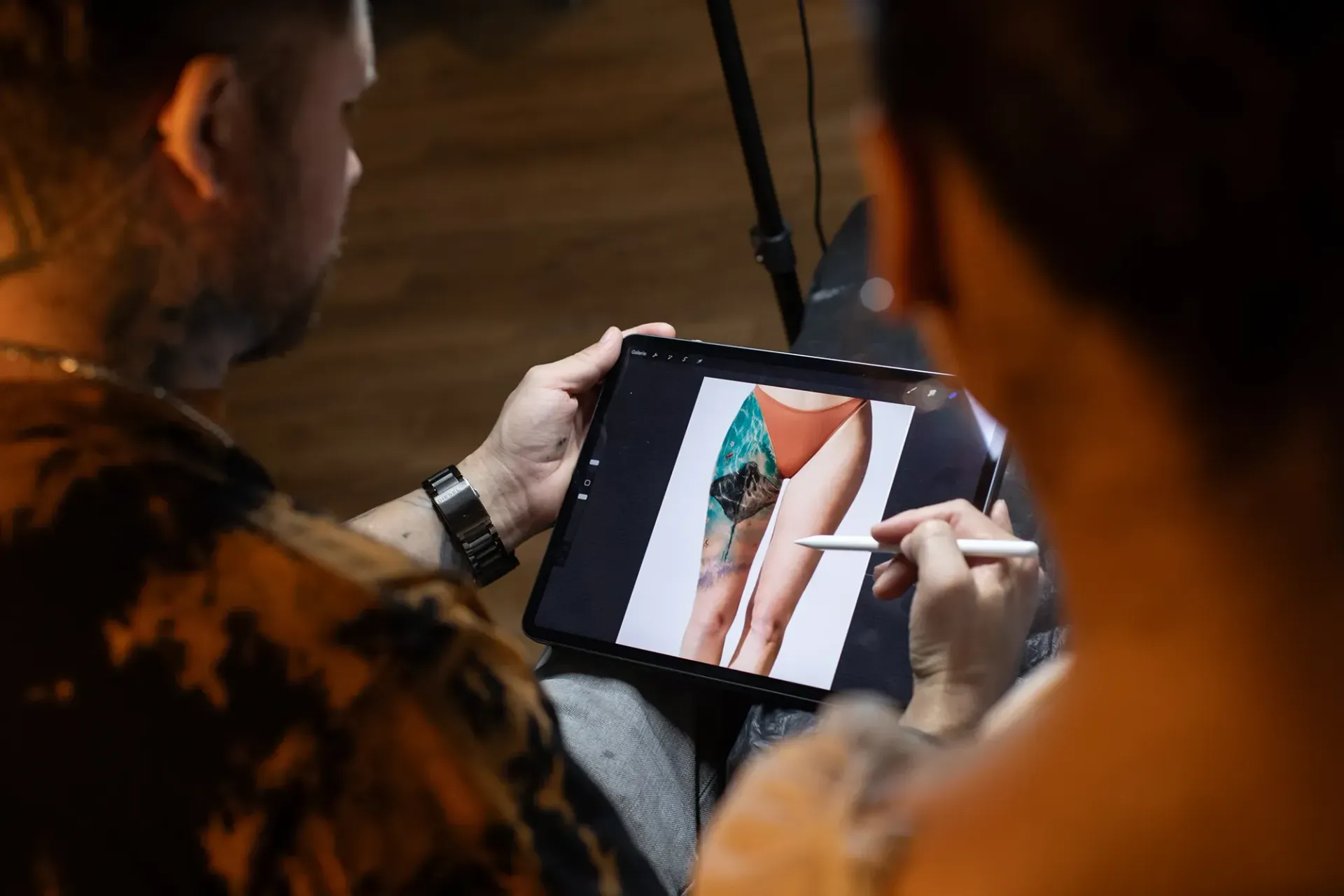 Ein Mann zeichnet mit einem Tablet ein Tattoo auf das Bein einer Frau.