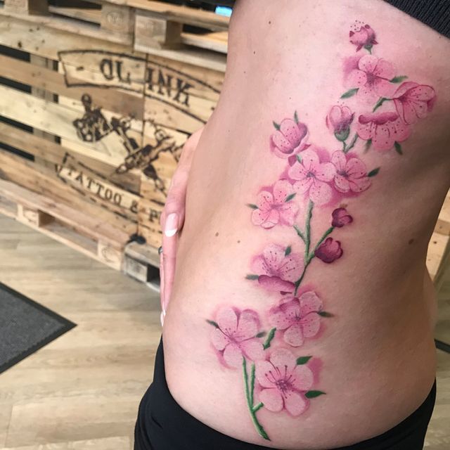 Eine Frau hat eine Tätowierung mit rosa Blumen auf ihrer Seite
