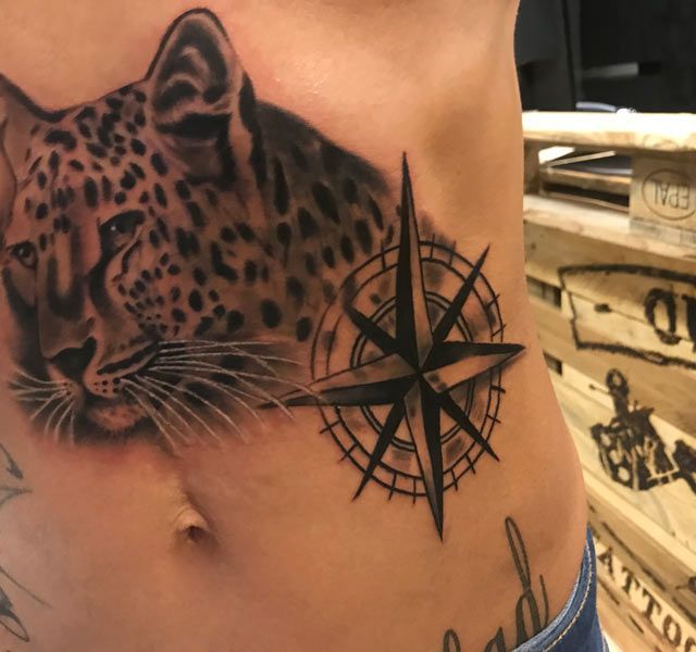 Ein Mann hat ein Tattoo von einem Leoparden und einem Kompass auf seiner Seite