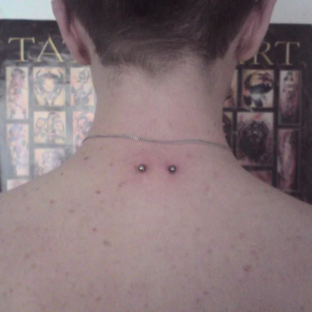 Eine Nahaufnahme des Rückens einer Person mit zwei Piercings darauf