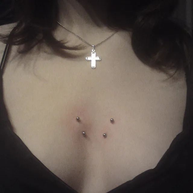 Eine Frau mit drei Piercings auf der Brust und einer Kreuzkette.