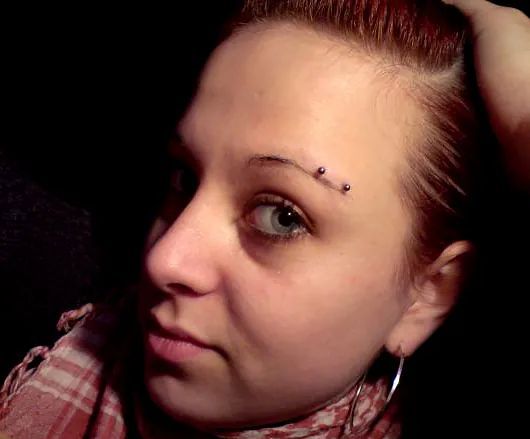 Eine Nahaufnahme des Gesichts einer Frau mit einem Piercing in ihrer Augenbraue.