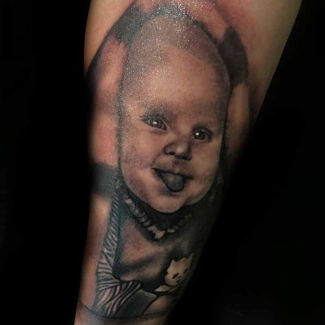 Eine schwarz-weiße Tätowierung eines Babys auf dem Arm einer Person.