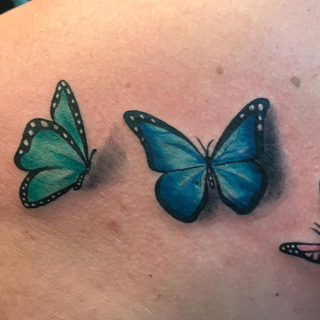 Drei blaue Schmetterlinge sind auf dem Rücken einer Frau tätowiert