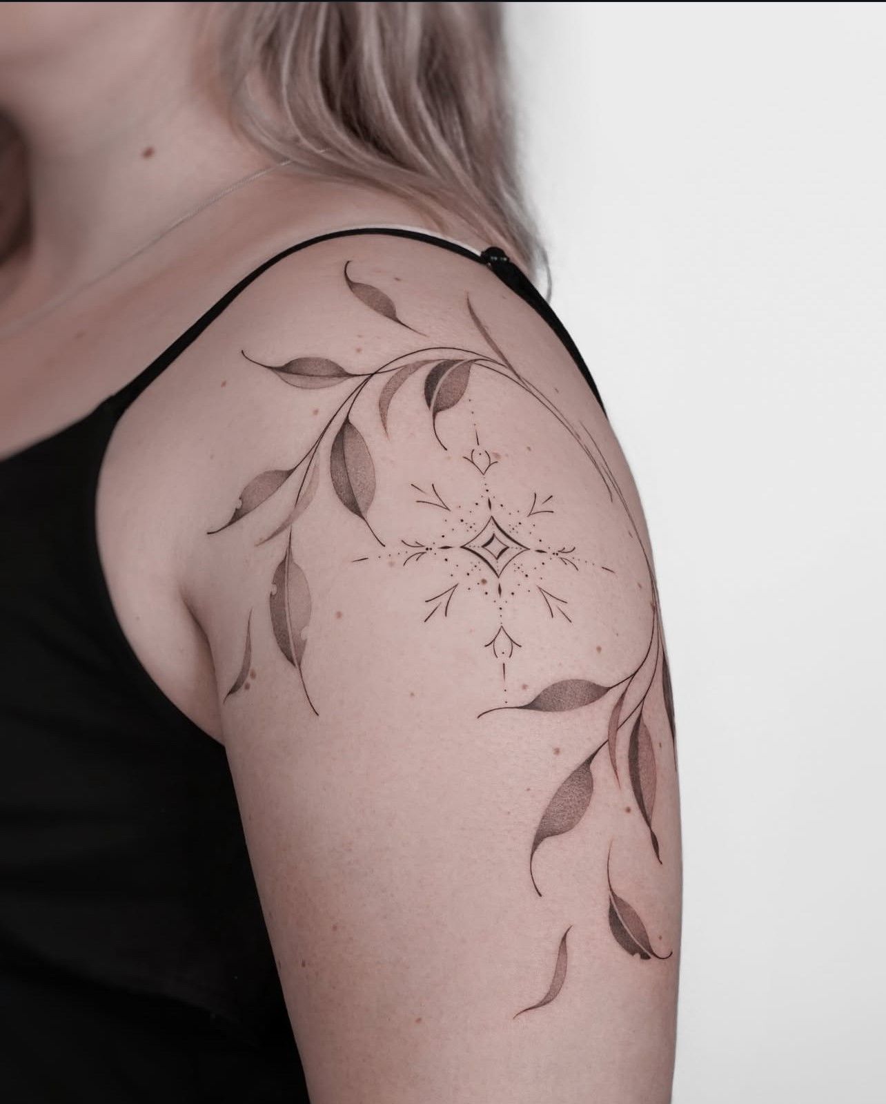 Eine Frau hat eine Blättertätowierung auf ihrer Schulter.