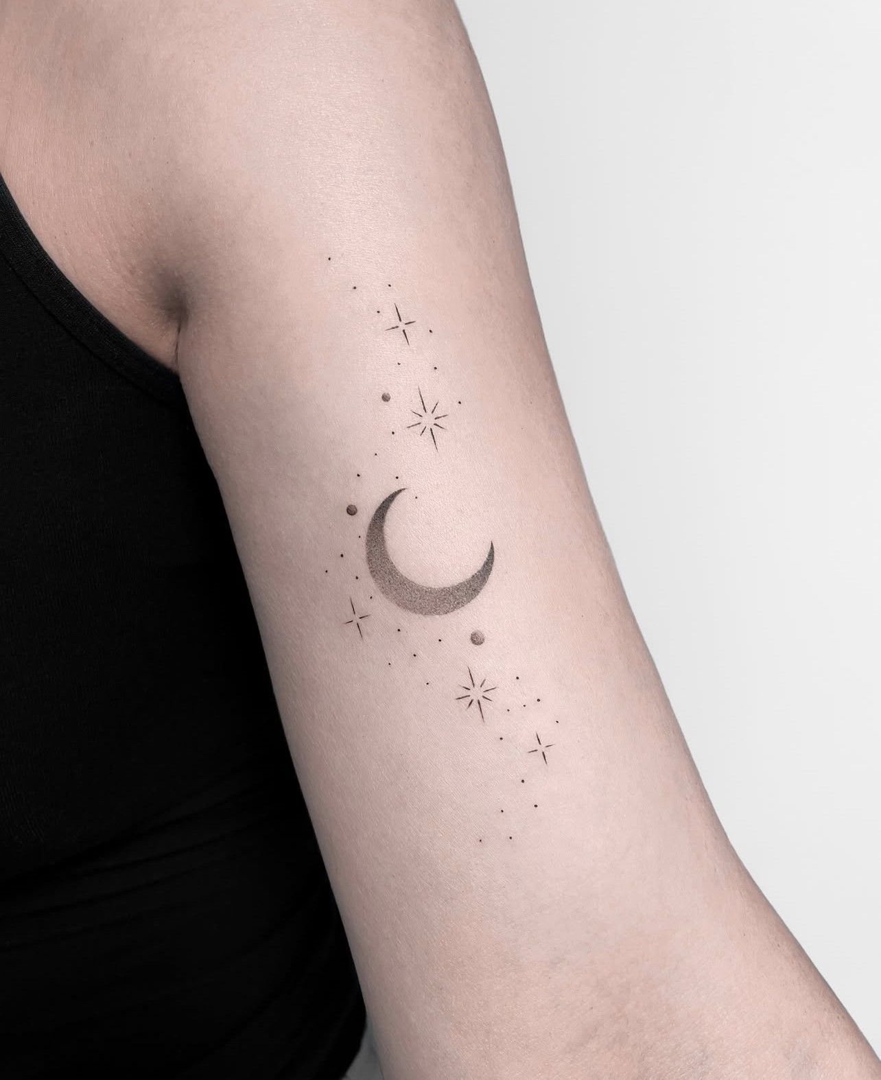 Eine Frau hat eine Tätowierung mit einer Mondsichel und Sternen auf ihrem Arm.