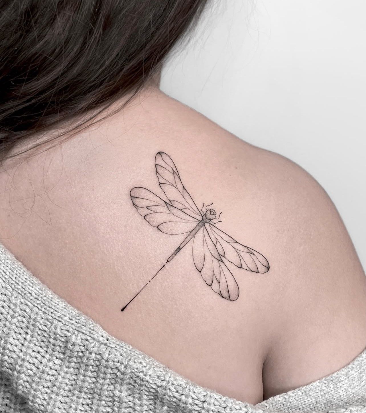 Eine Frau hat eine Libellentätowierung auf ihrem Rücken.