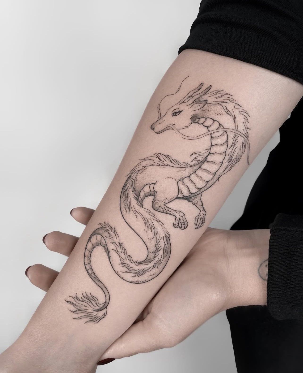 Eine Person hat eine Drachentätowierung auf dem Unterarm