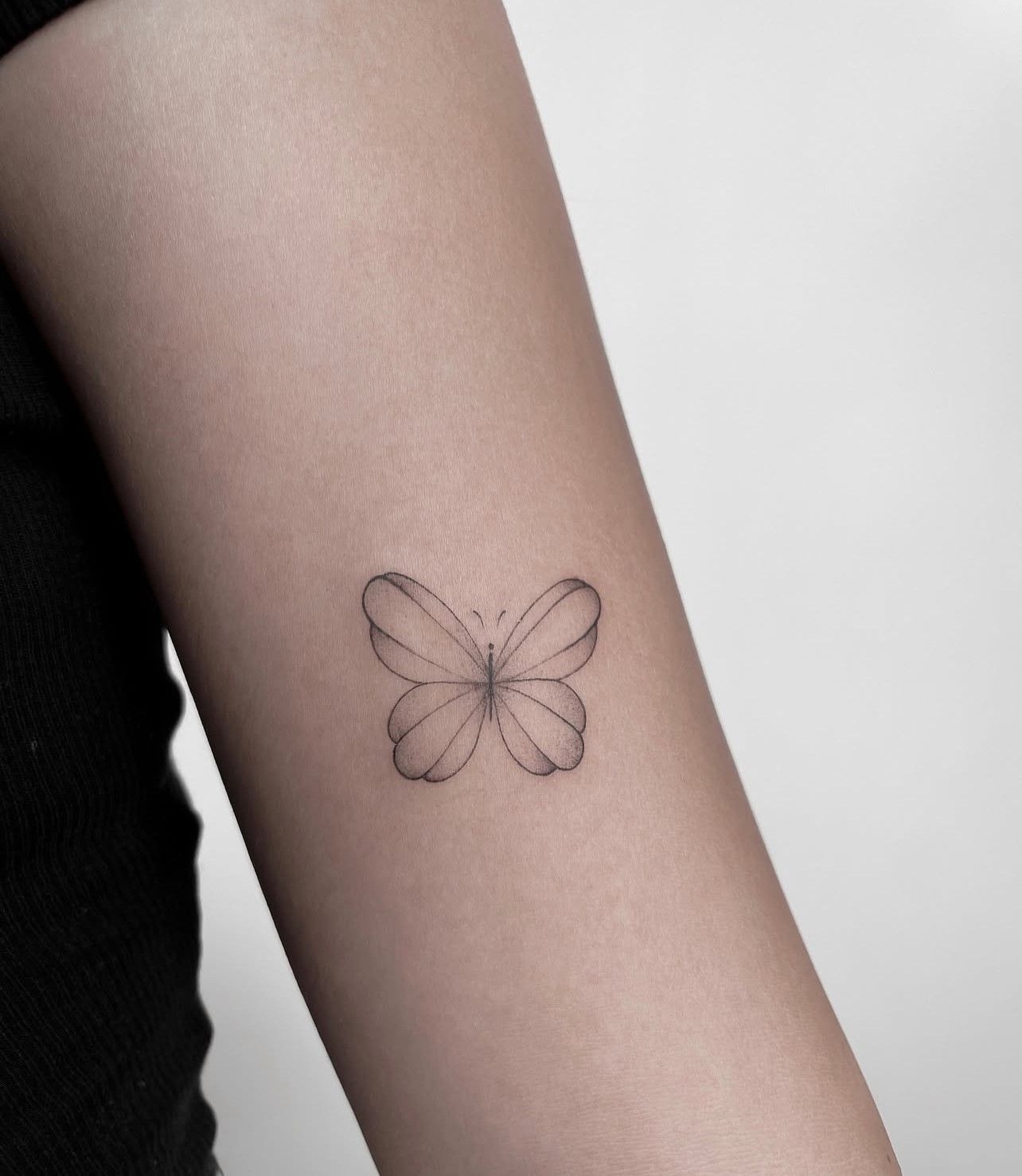 Eine Frau hat ein kleines Schmetterlingstattoo auf ihrem Arm