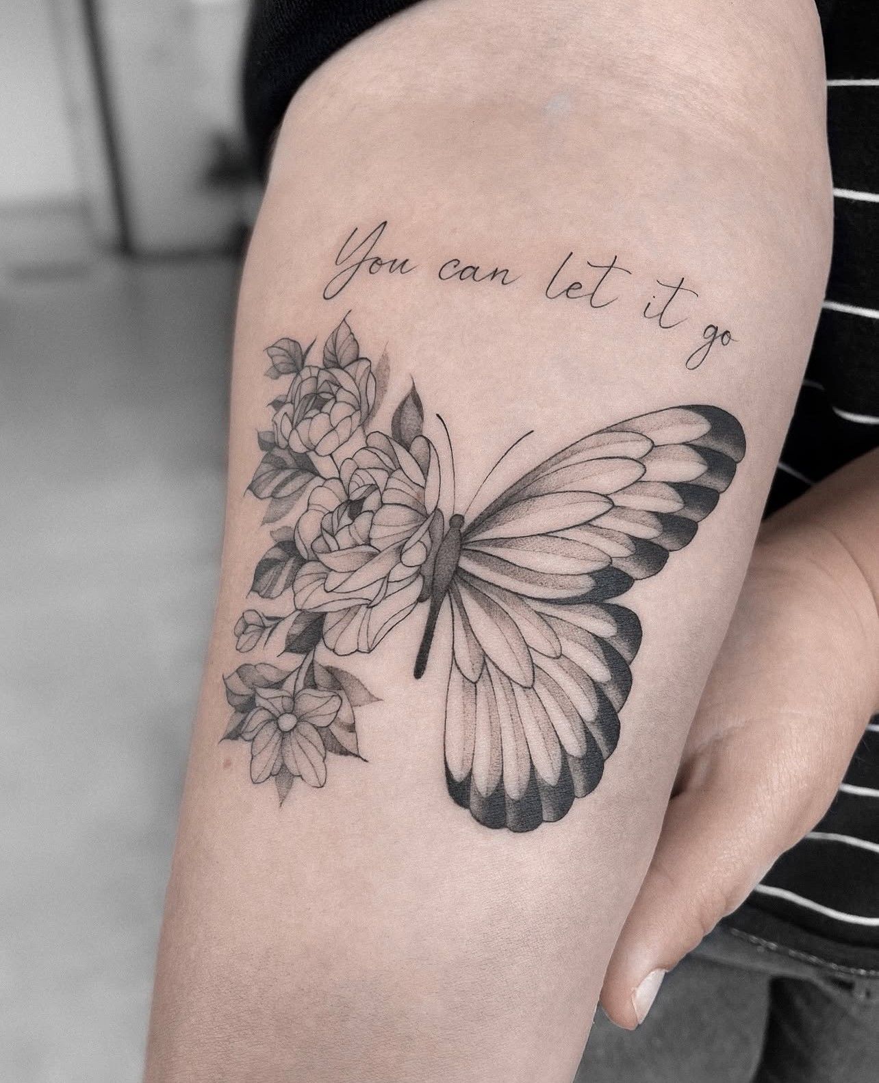 Eine Frau hat ein Tattoo mit einem Schmetterling und Blumen auf ihrem Arm.