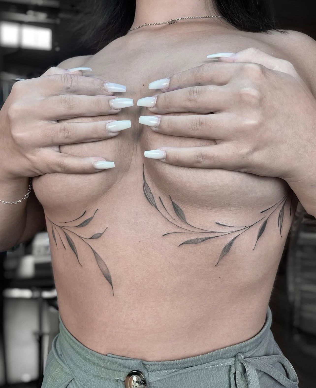 Eine Frau mit weißen Nägeln hat eine Tätowierung auf der Brust.