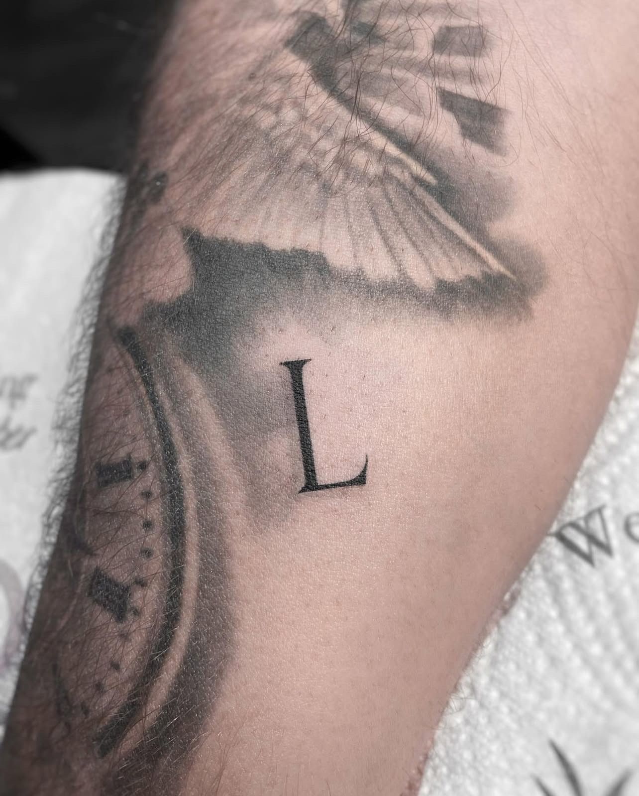 Ein Mann hat eine Uhr und den Buchstaben L auf seinem Unterarm tätowiert.
