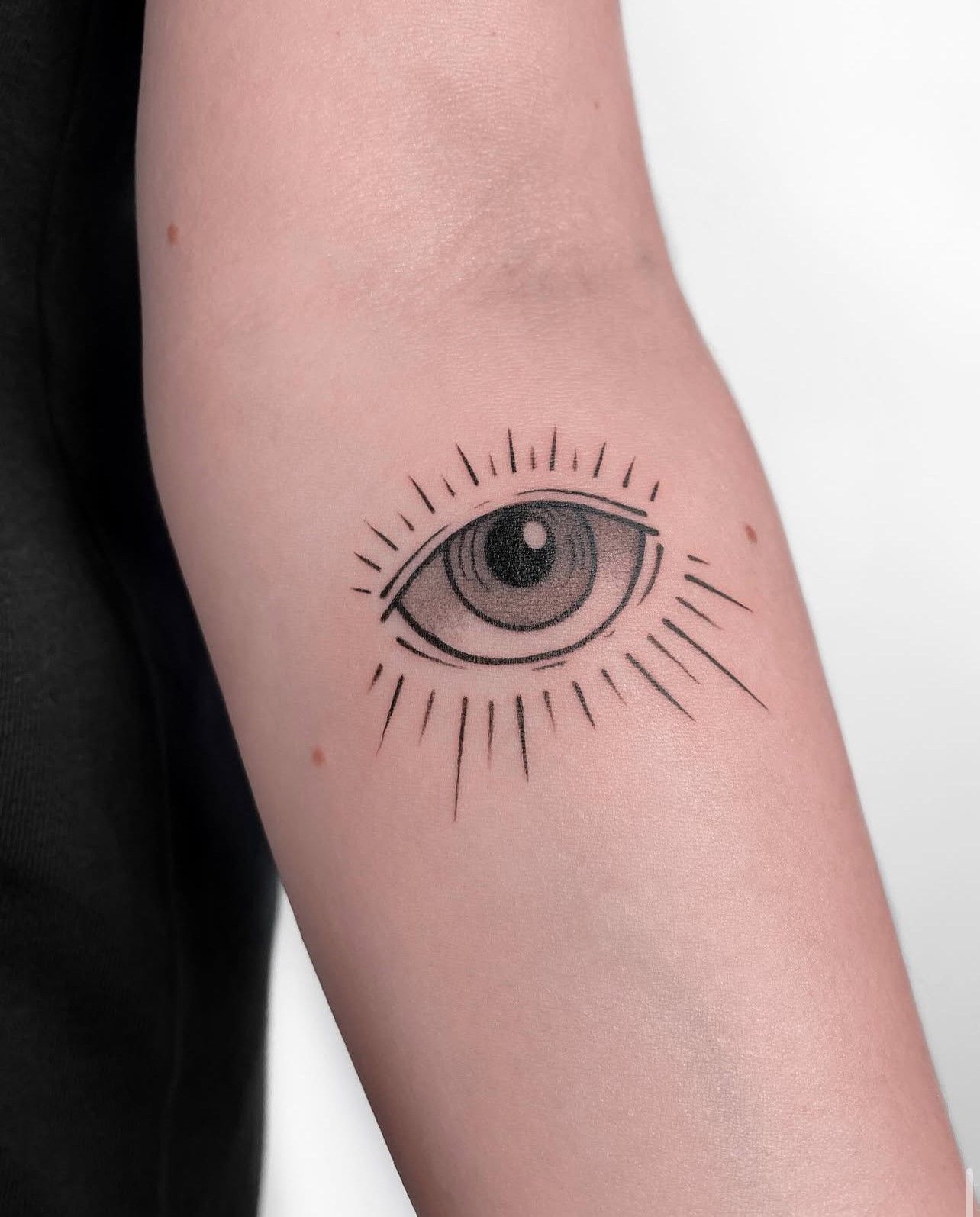 Eine Frau hat ein Tattoo mit einem bösen Blick auf ihrem Unterarm.