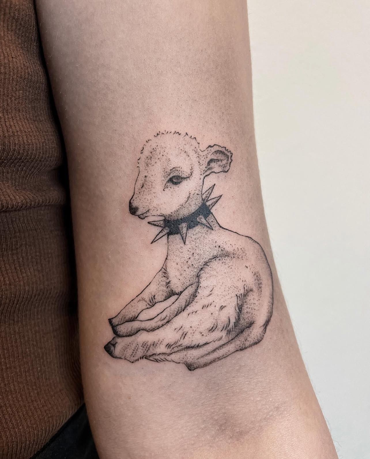 Eine Person hat eine Tätowierung eines Lamms auf dem Arm.