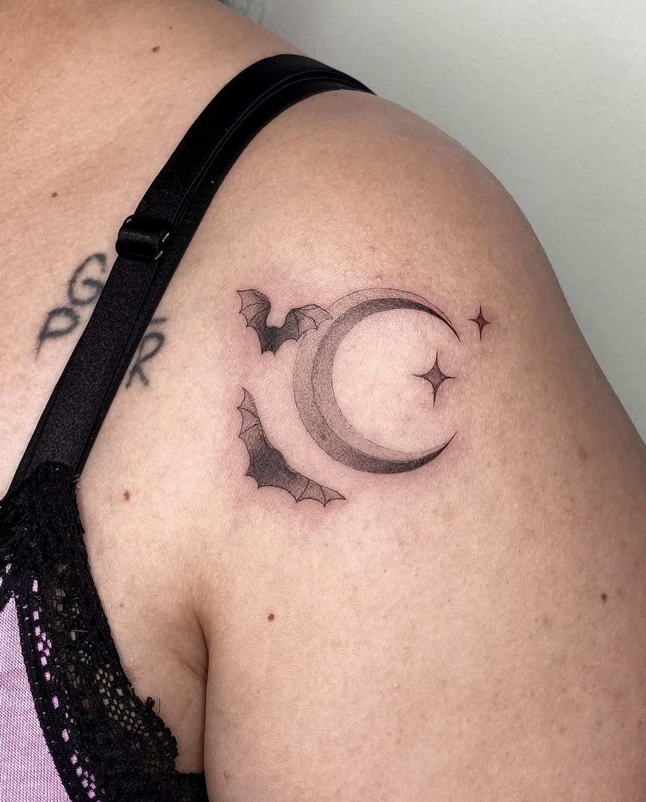 Eine Frau hat eine Tätowierung einer Fledermaus und einer Mondsichel auf ihrer Schulter.