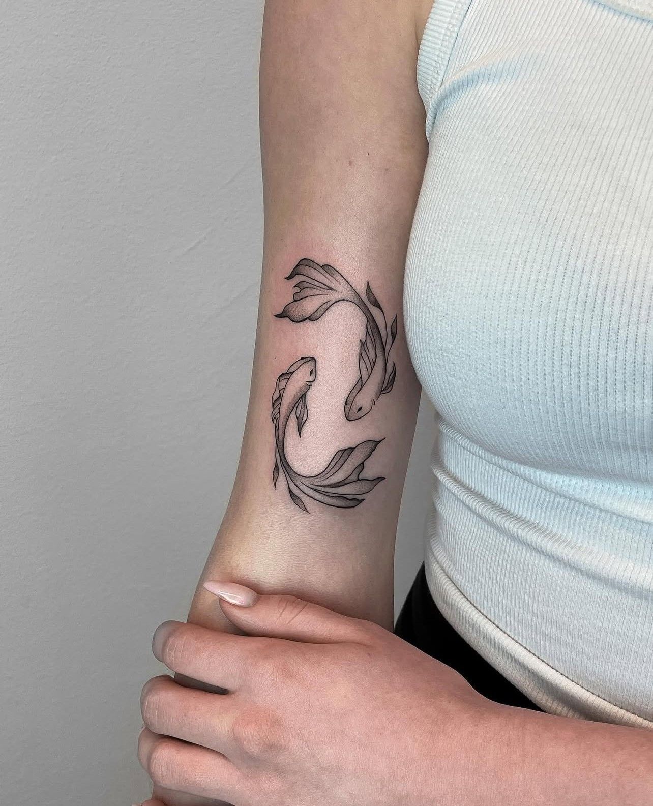Eine Frau hat eine Tätowierung mit zwei Fischen auf ihrem Arm.
