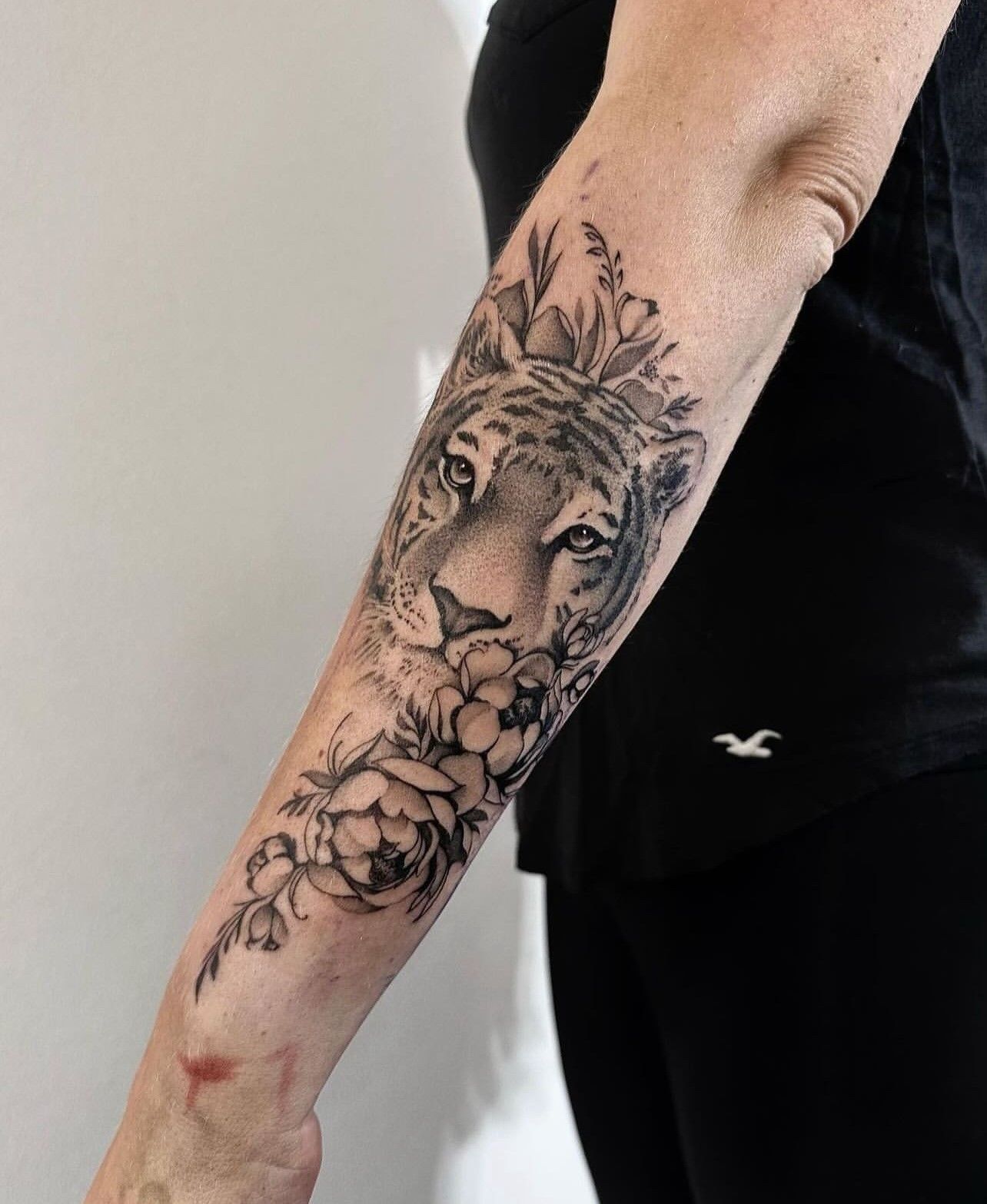 Eine Frau hat ein Tattoo mit einem Tiger und Blumen auf ihrem Unterarm.