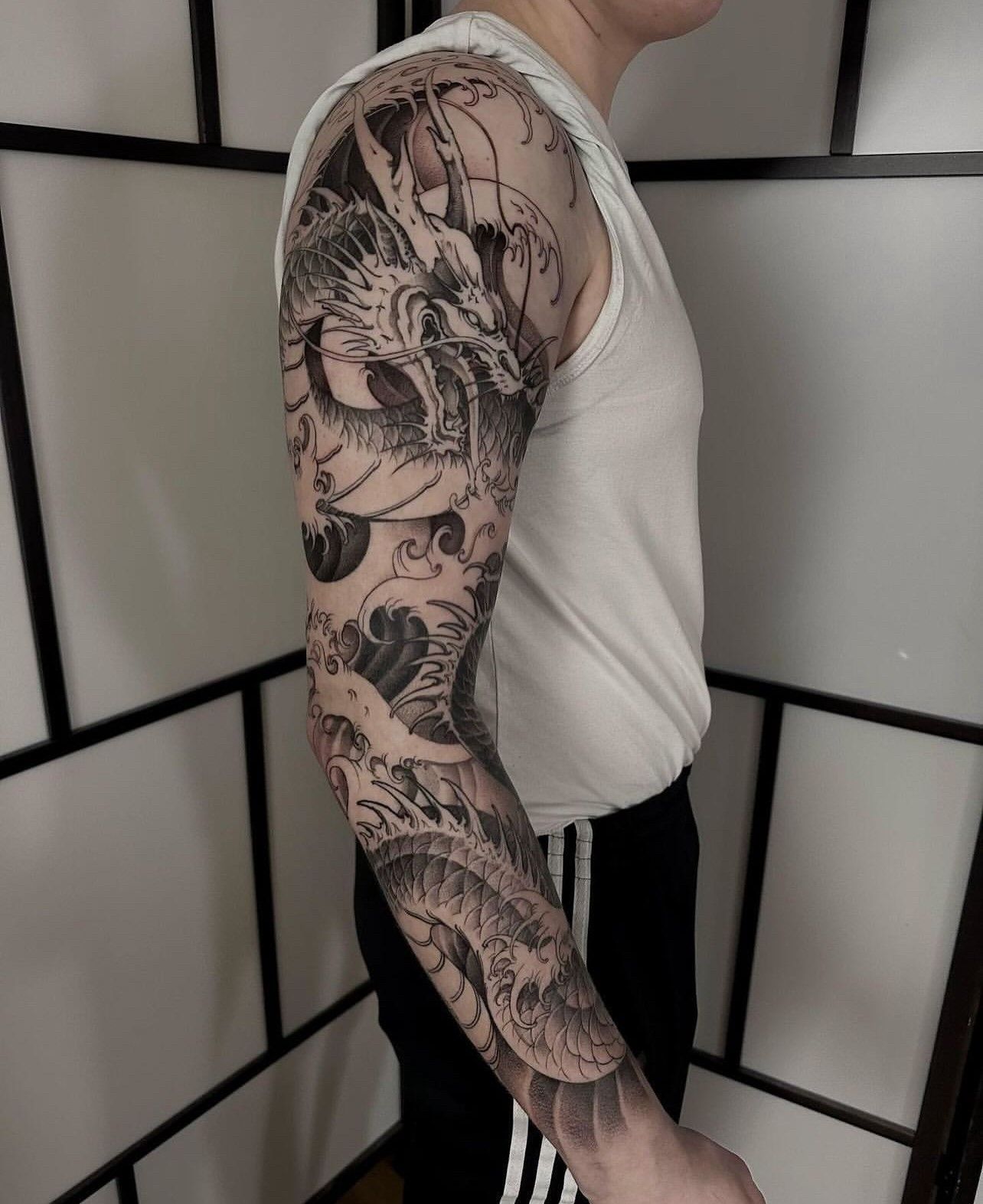 Ein Mann hat ein Drachentattoo auf dem ganzen Arm.